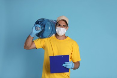 Photo of Courier in medical mask with bottle for water cooler and clipboard on light blue background. Delivery during coronavirus quarantine