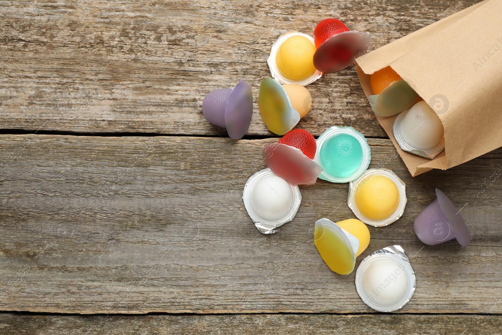 Photo of Paper bag with tasty bright jelly cups on wooden table, flat lay. Space for text