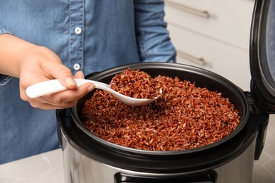 Woman taking delicious brown rice from multi cooker indoors, closeup