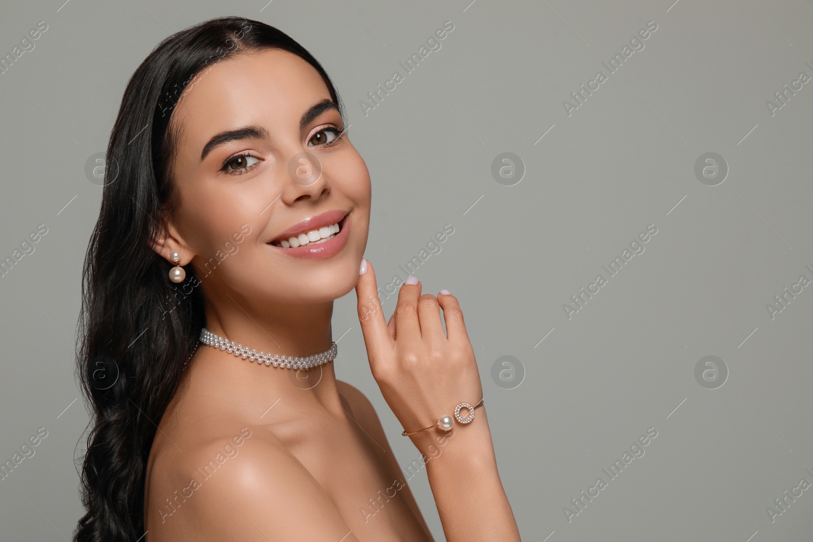 Photo of Young woman wearing elegant pearl jewelry on grey background, space for text