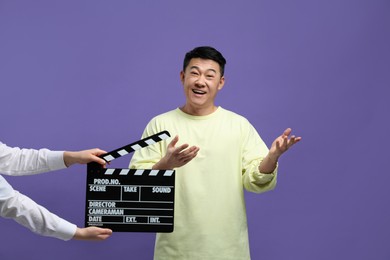 Photo of Happy asian actor performing while second assistant camera holding clapperboard on purple background. Film industry