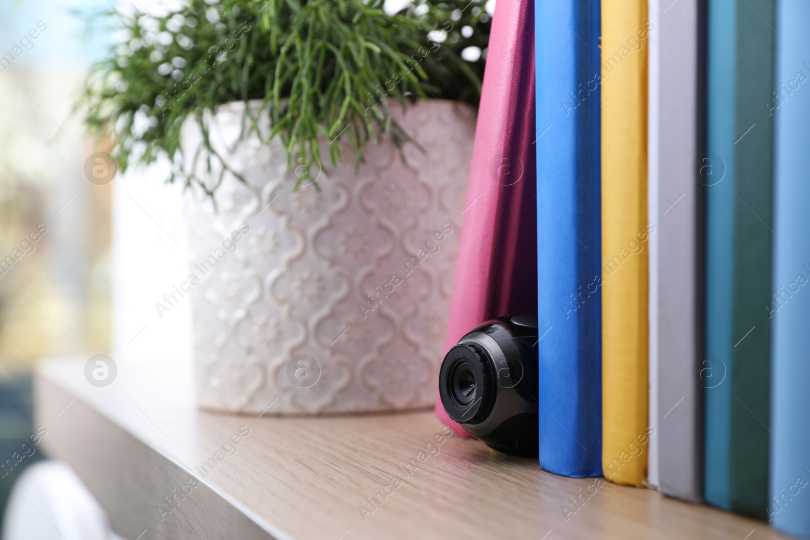 Photo of Camera hidden between books on wooden shelf indoors, closeup. Space for text