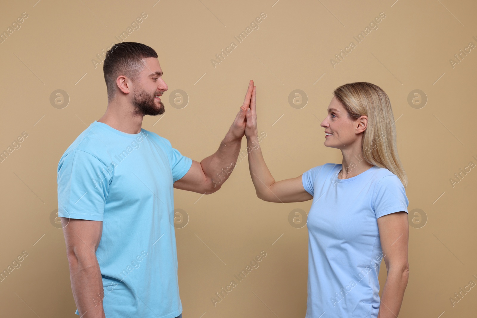 Photo of Happy couple giving high five on light brown background