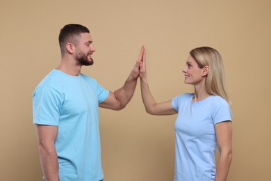 Happy couple giving high five on light brown background