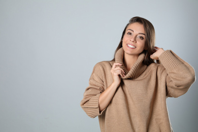 Photo of Young woman in stylish brown sweater on grey background, space for text