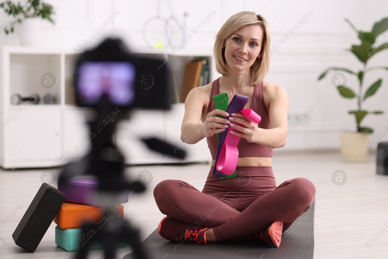 Photo of Smiling sports blogger with with resistance bands recording fitness lesson with camera at home