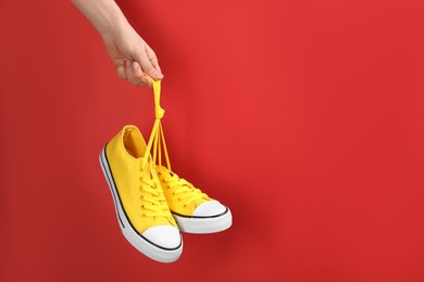 Photo of Woman holding pair of sneakers on red background, closeup. Space for text