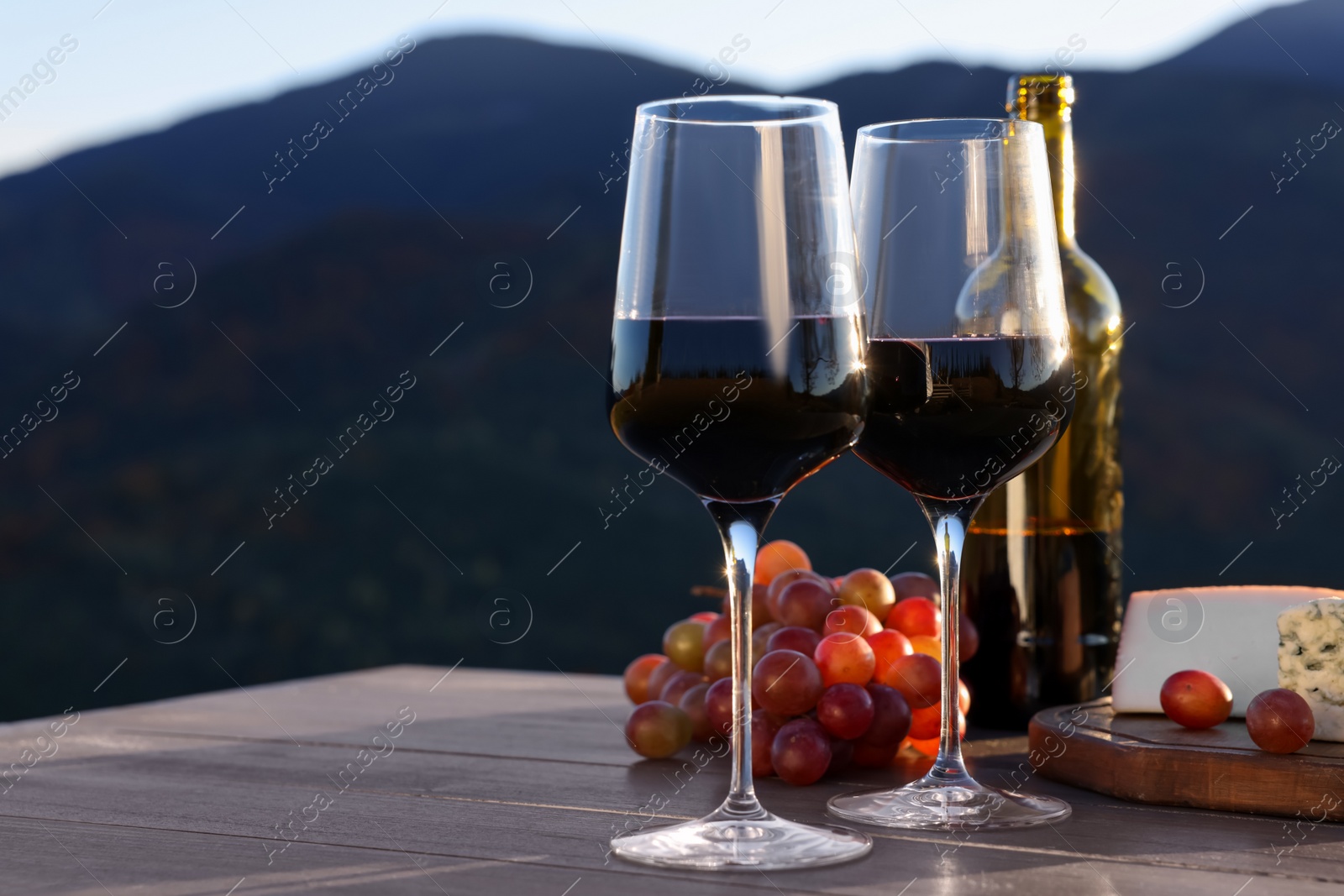 Photo of Red wine served with cheese and grapes on wooden table against mountain landscape
