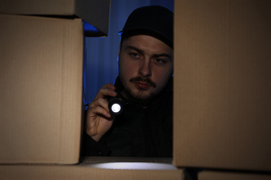 Security guard with flashlight looking through pile of cardboard boxes in dark room