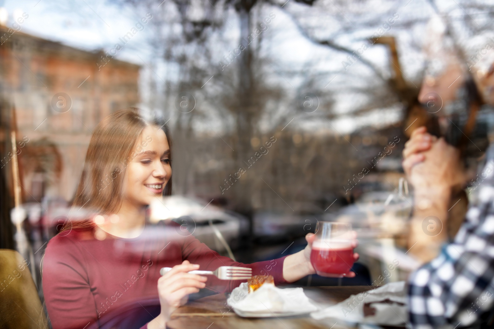 Photo of Lovely young couple spending time together in cafe, view from outdoors through window