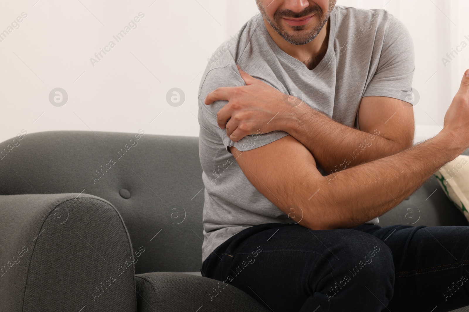 Photo of Man suffering from pain in his shoulder on sofa indoors, closeup