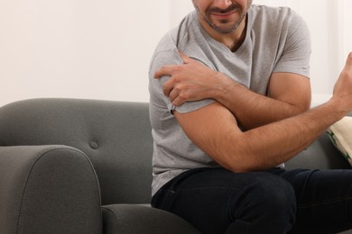 Man suffering from pain in his shoulder on sofa indoors, closeup