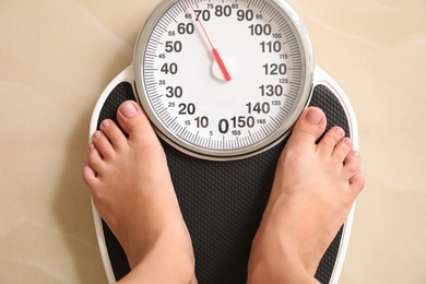 Photo of Woman standing on floor scales indoors, top view. Overweight problem