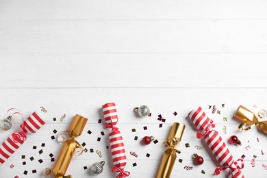 Photo of Christmas crackers with decorations and shiny confetti on white wooden background, flat lay. Space for text