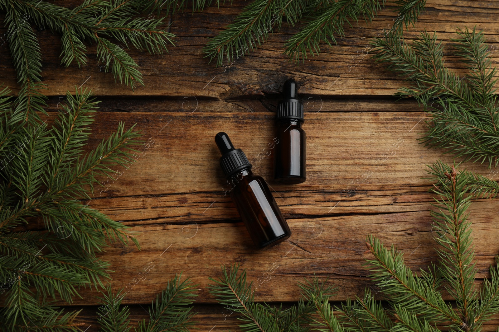 Photo of Pine essential oil and branches on wooden table, flat lay