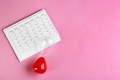 Photo of Calendar and hourglass on pink background, flat lay. Space for text
