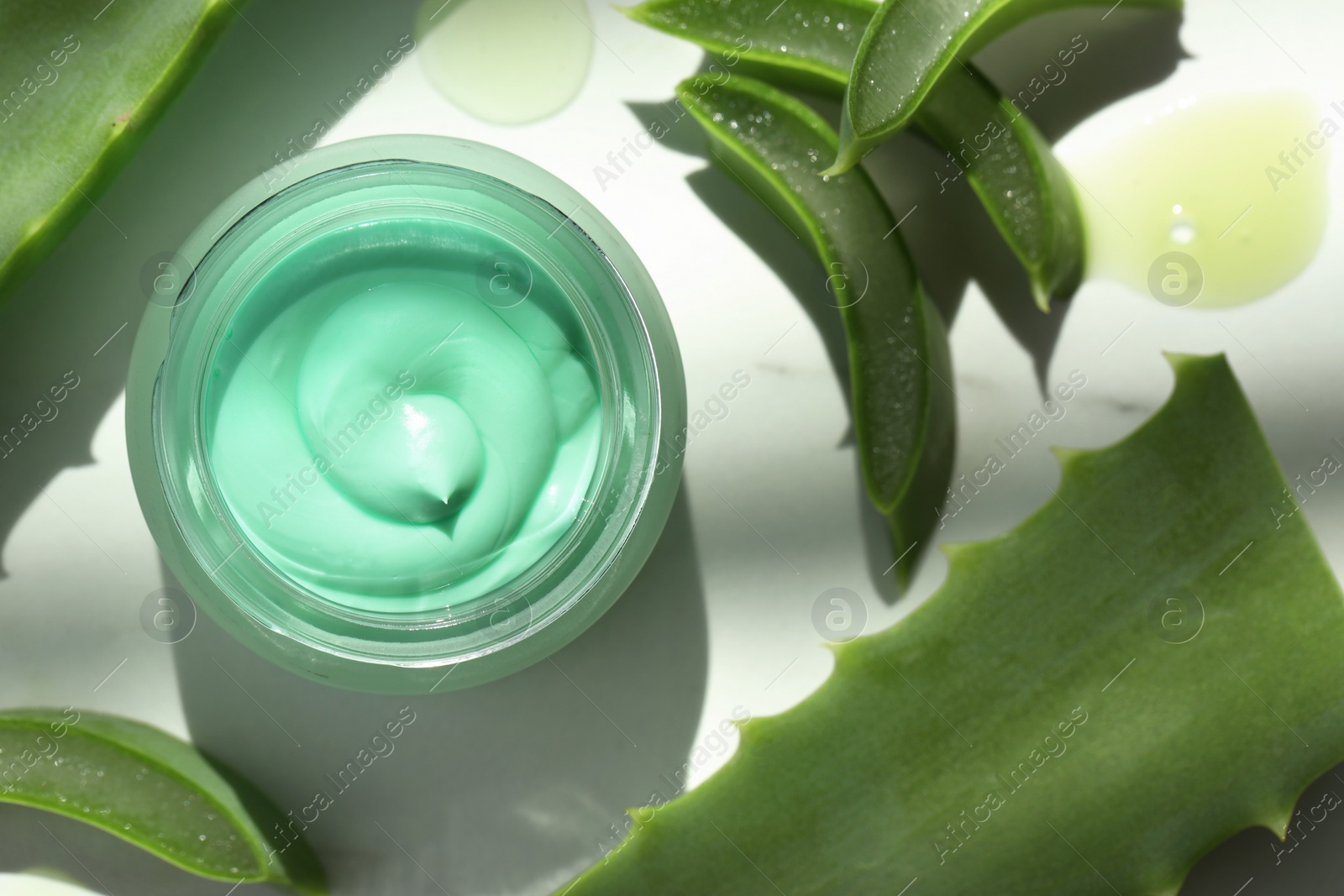 Photo of Jar with cream and cut aloe leaves on white table, flat lay