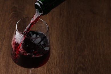 Photo of Pouring tasty red wine in glass at wooden table, closeup. Space for text