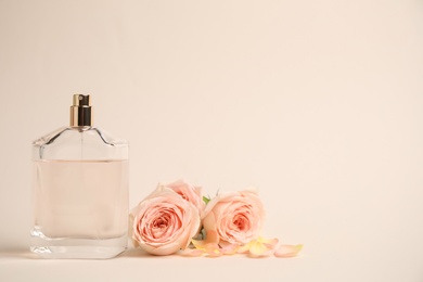 Photo of Bottle of perfume with roses on beige background, space for text