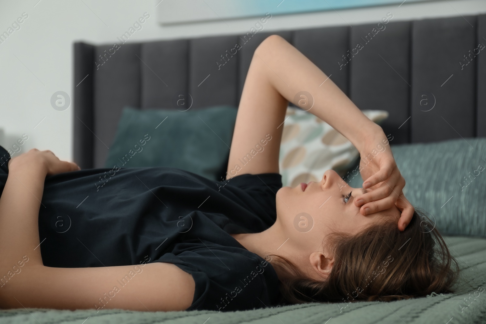 Photo of Sad young woman lying on bed at home