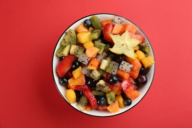 Photo of Delicious exotic fruit salad on red background, top view
