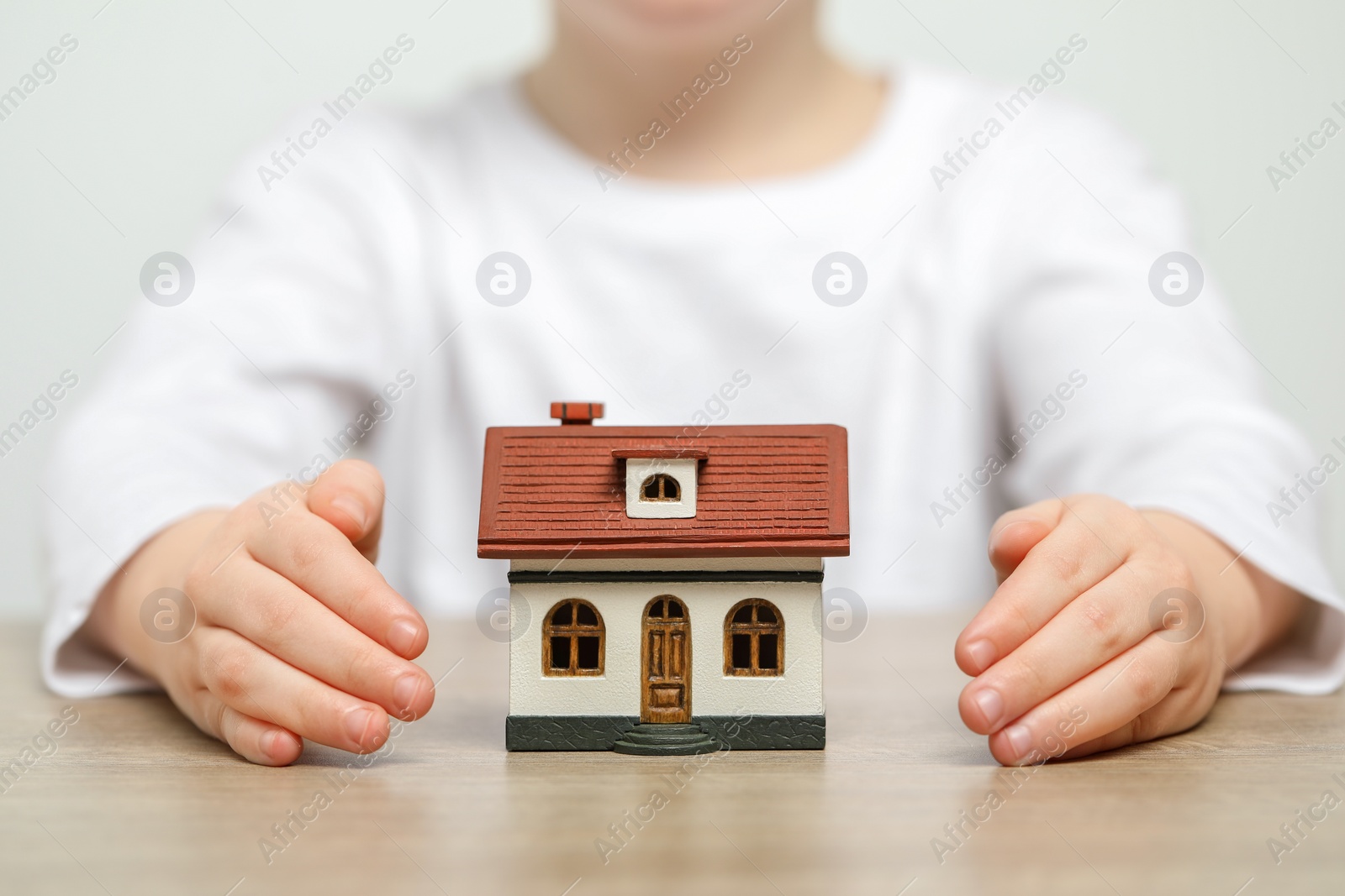 Photo of Home security concept. Little child with house model at wooden table, closeup