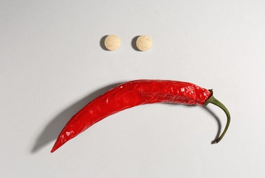 Photo of Sad face made of chili pepper and pills on light grey background, flat lay. Potency problem