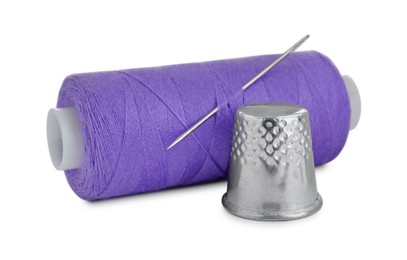 Photo of Thimble and spool of purple sewing thread with needle isolated on white