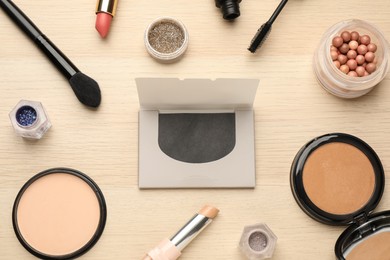 Photo of Facial oil blotting tissues and different decorative cosmetics on wooden table, flat lay. Mattifying wipes