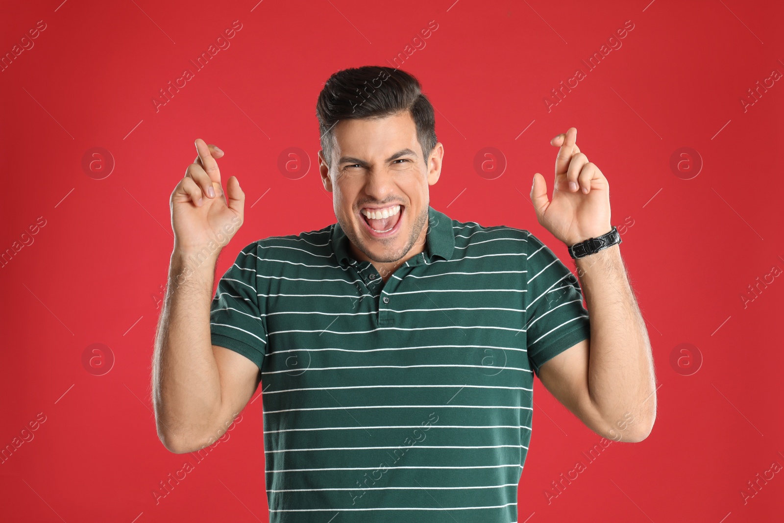 Photo of Man with crossed fingers on red background. Superstition concept