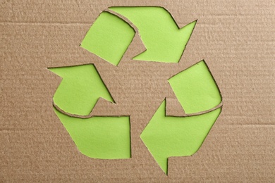 Photo of Sheet of cardboard with cutout recycling symbol on green background, top view