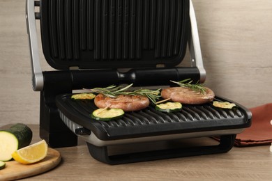 Photo of Electric grill with homemade sausages, zucchini and rosemary on wooden table