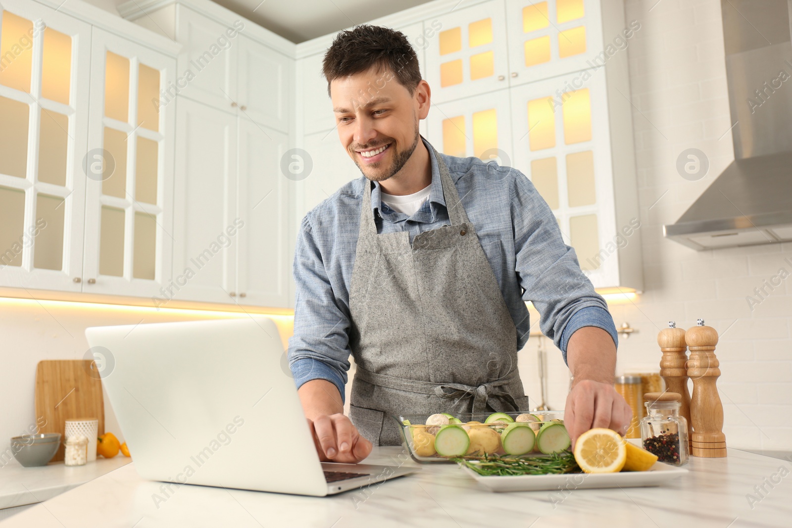 Photo of Man making dinner while watching online cooking course via laptop kitchen