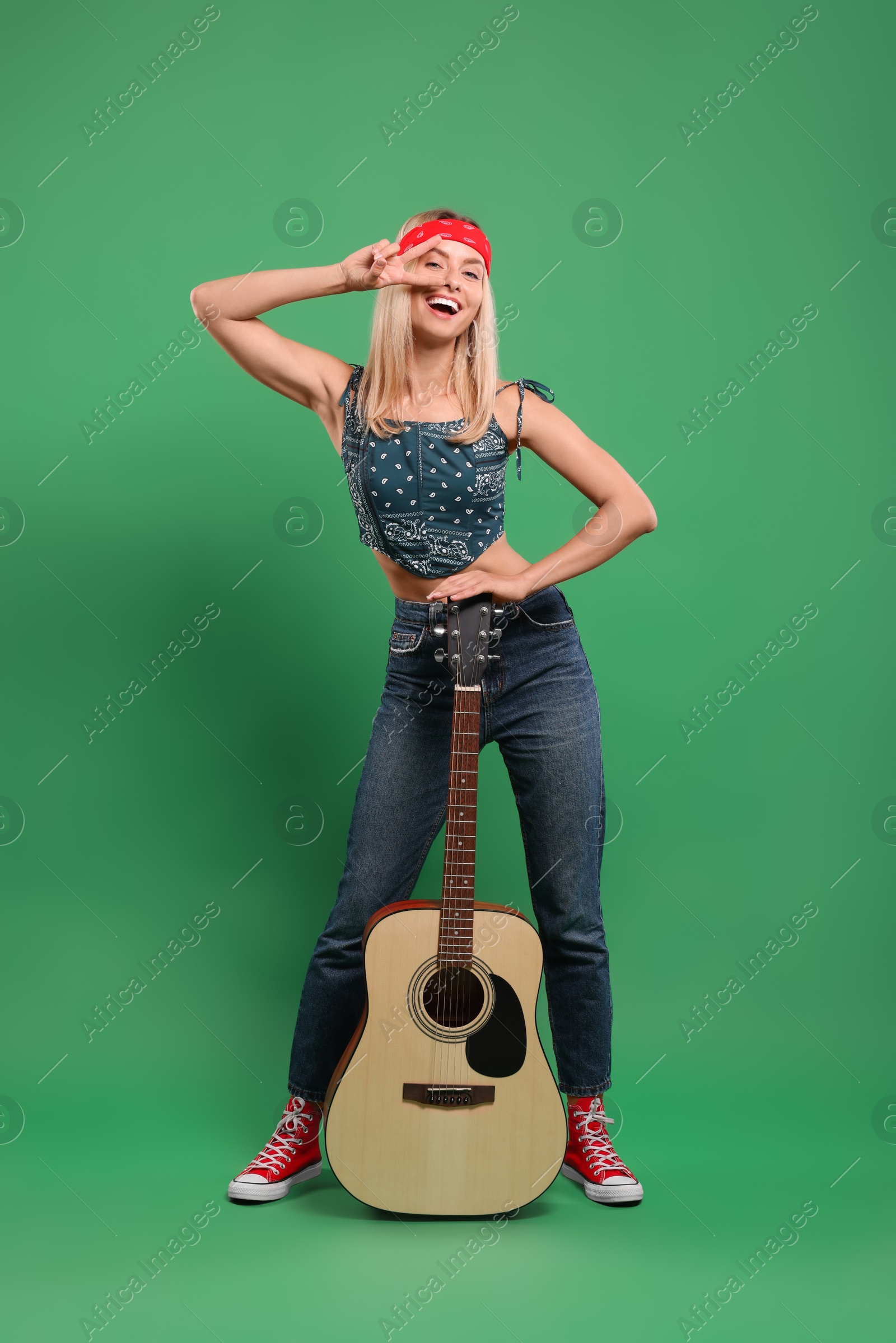 Photo of Happy hippie woman with guitar showing peace sign on green background