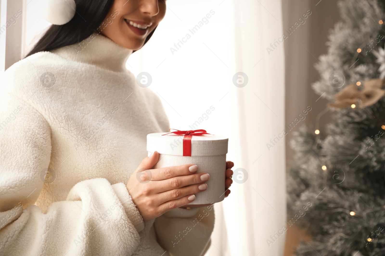 Photo of Woman holding gift box near Christmas tree, closeup