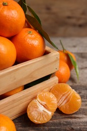 Delicious tangerines with leaves on wooden table, closeup