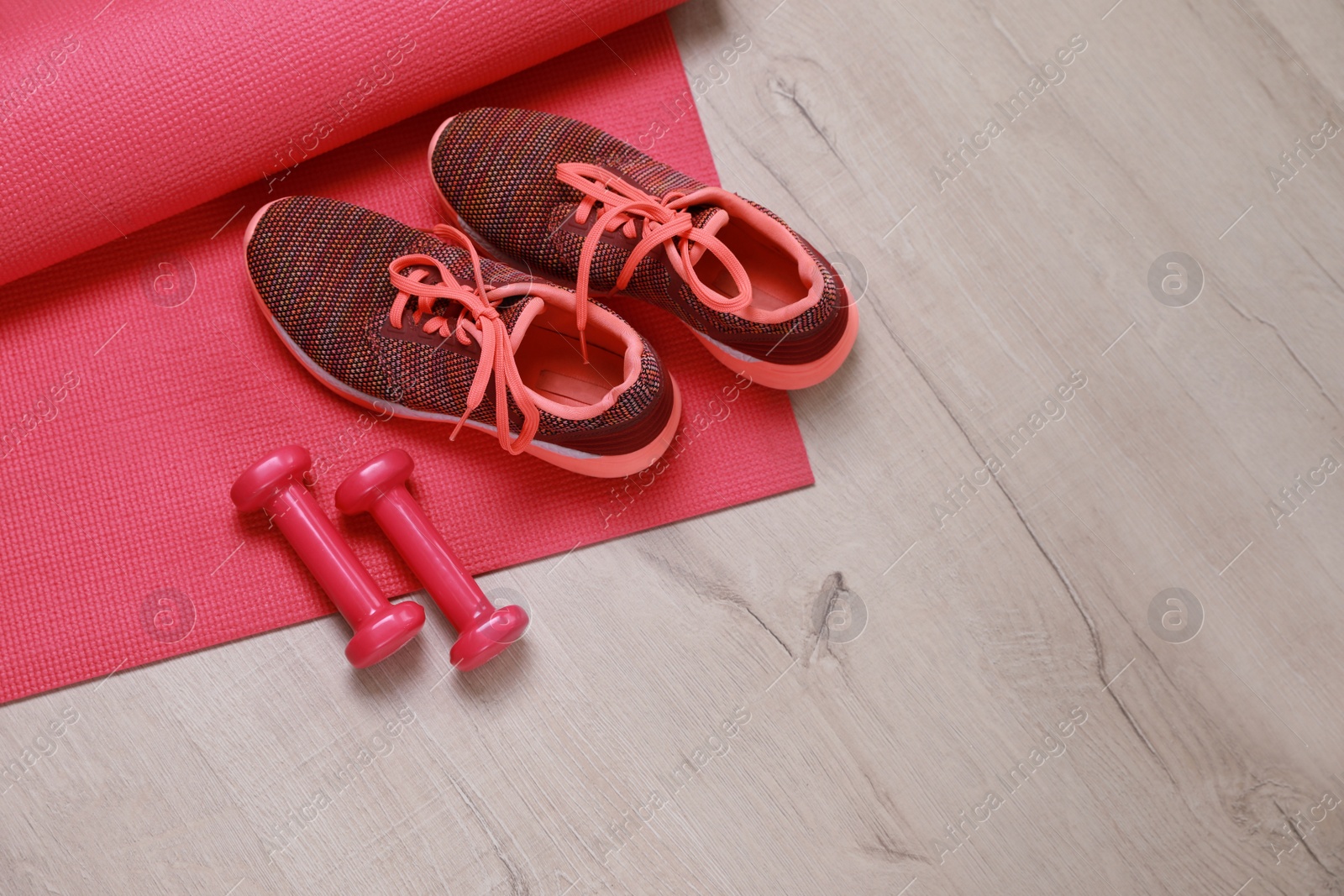 Photo of Dumbbells, sneakers and mat on wooden floor, above view. Space for text