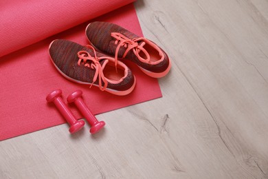 Photo of Dumbbells, sneakers and mat on wooden floor, above view. Space for text