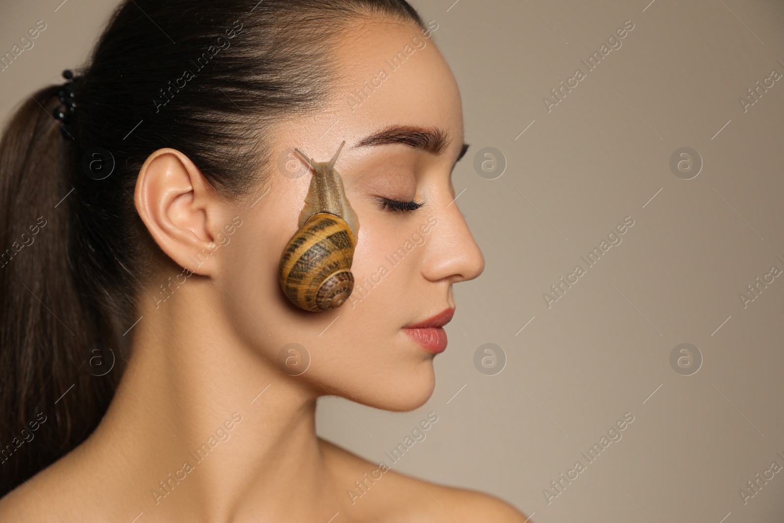 Photo of Beautiful young woman with snail on her face against beige background. Space for text