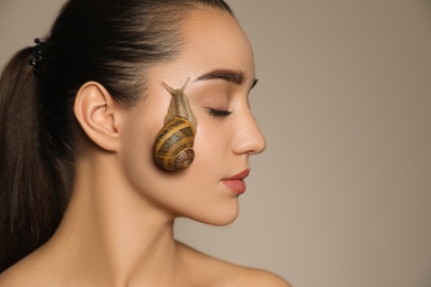 Beautiful young woman with snail on her face against beige background. Space for text