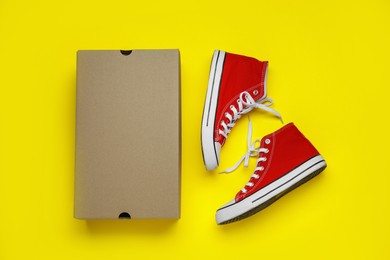 Photo of Comfortable shoes and cardboard box on yellow background, flat lay. Space for text