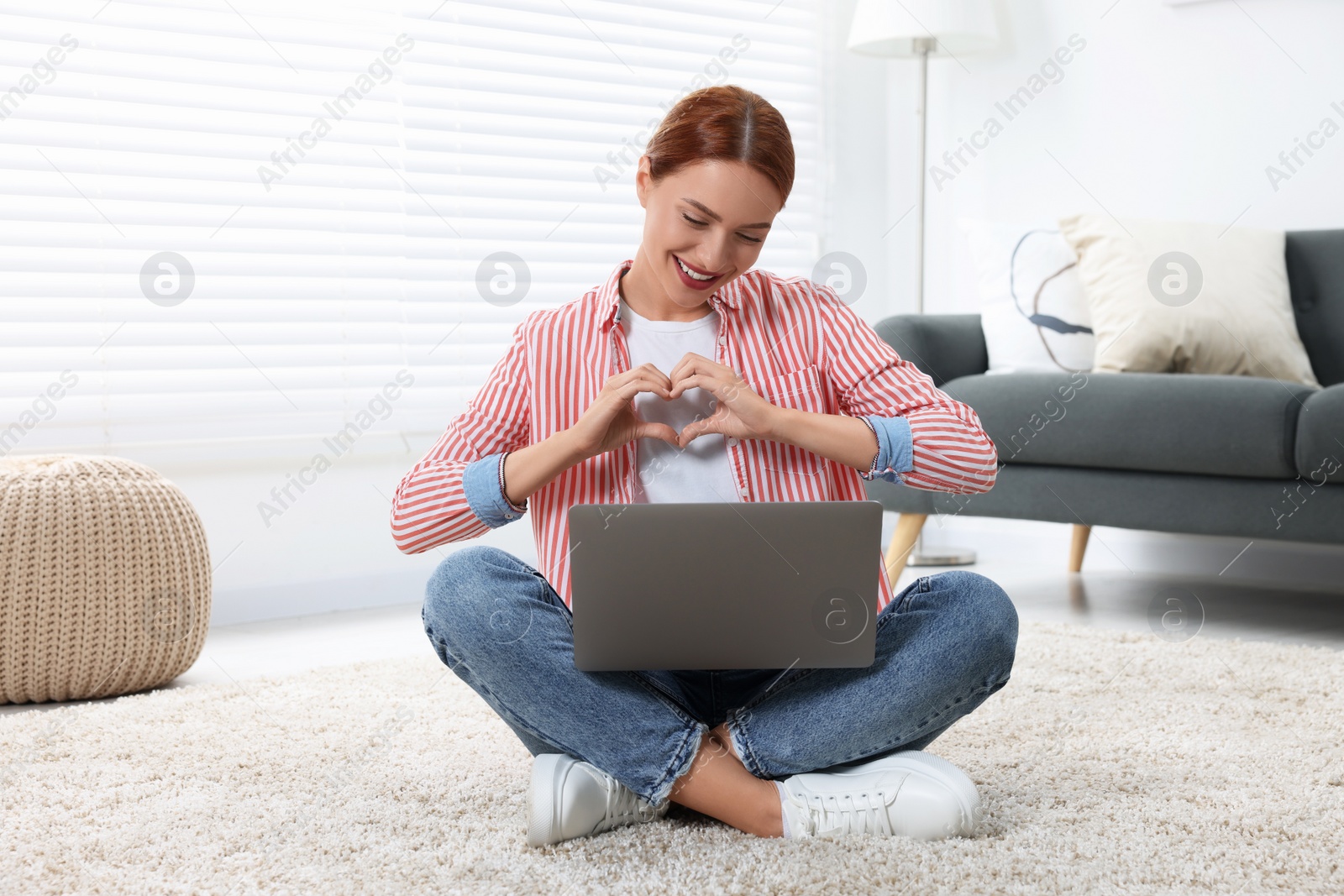 Photo of Woman making heart with hands during video chat via laptop at home. Long-distance relationship