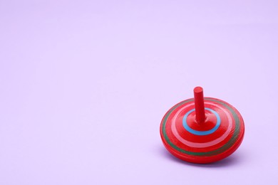Photo of One bright spinning top on lilac background, space for text. Toy whirligig