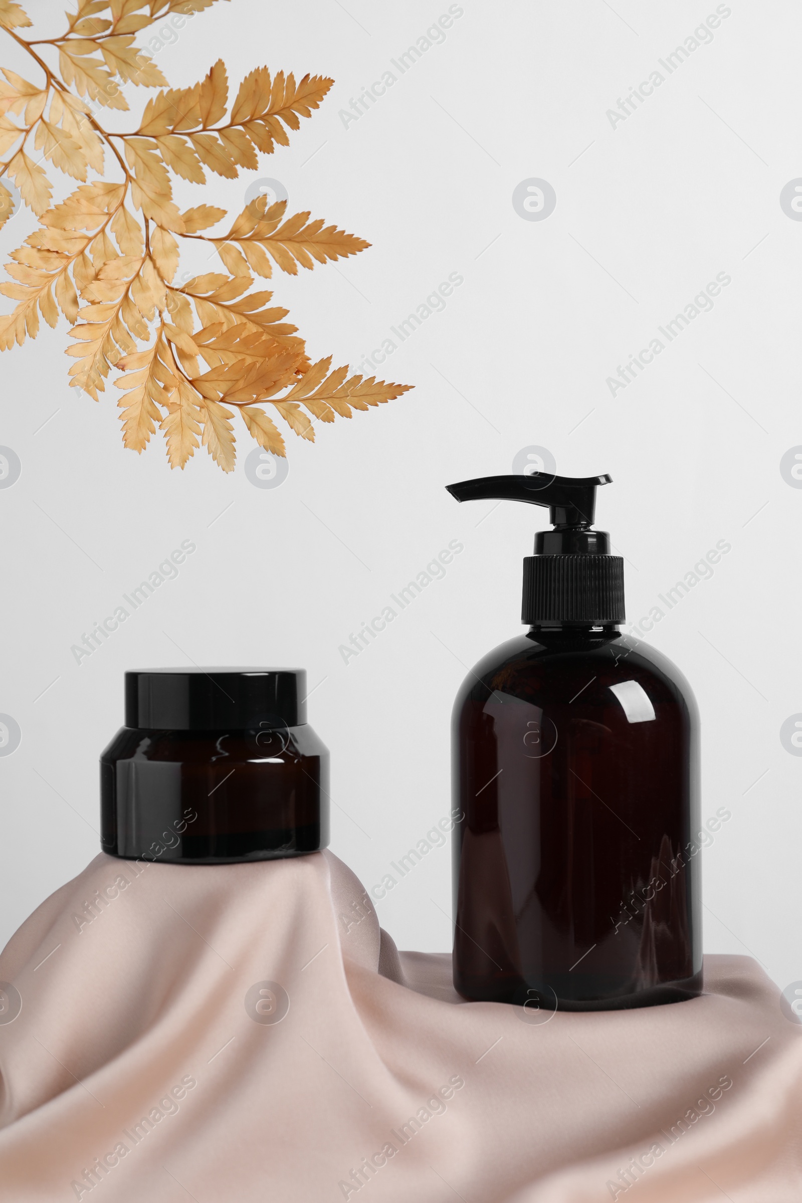 Photo of Different cosmetic product and dry leaves on pink fabric