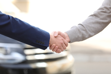 Photo of Salesman shaking hands with customer in modern auto dealership, closeup. Buying new car