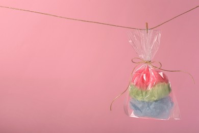 Photo of Packaged sweet cotton candy hanging on clothesline against pink background, space for text