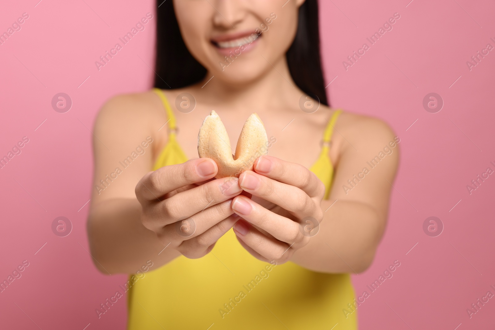 Photo of Young woman holding tasty fortune cookie with prediction on pink background, closeup