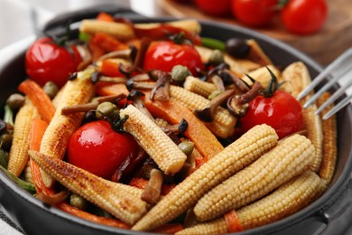 Tasty roasted baby corn with tomatoes, capers and mushrooms in frying pan, closeup