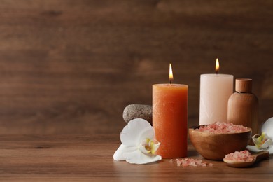 Beautiful spa composition with sea salt, burning candles and flowers on wooden table. Space for text