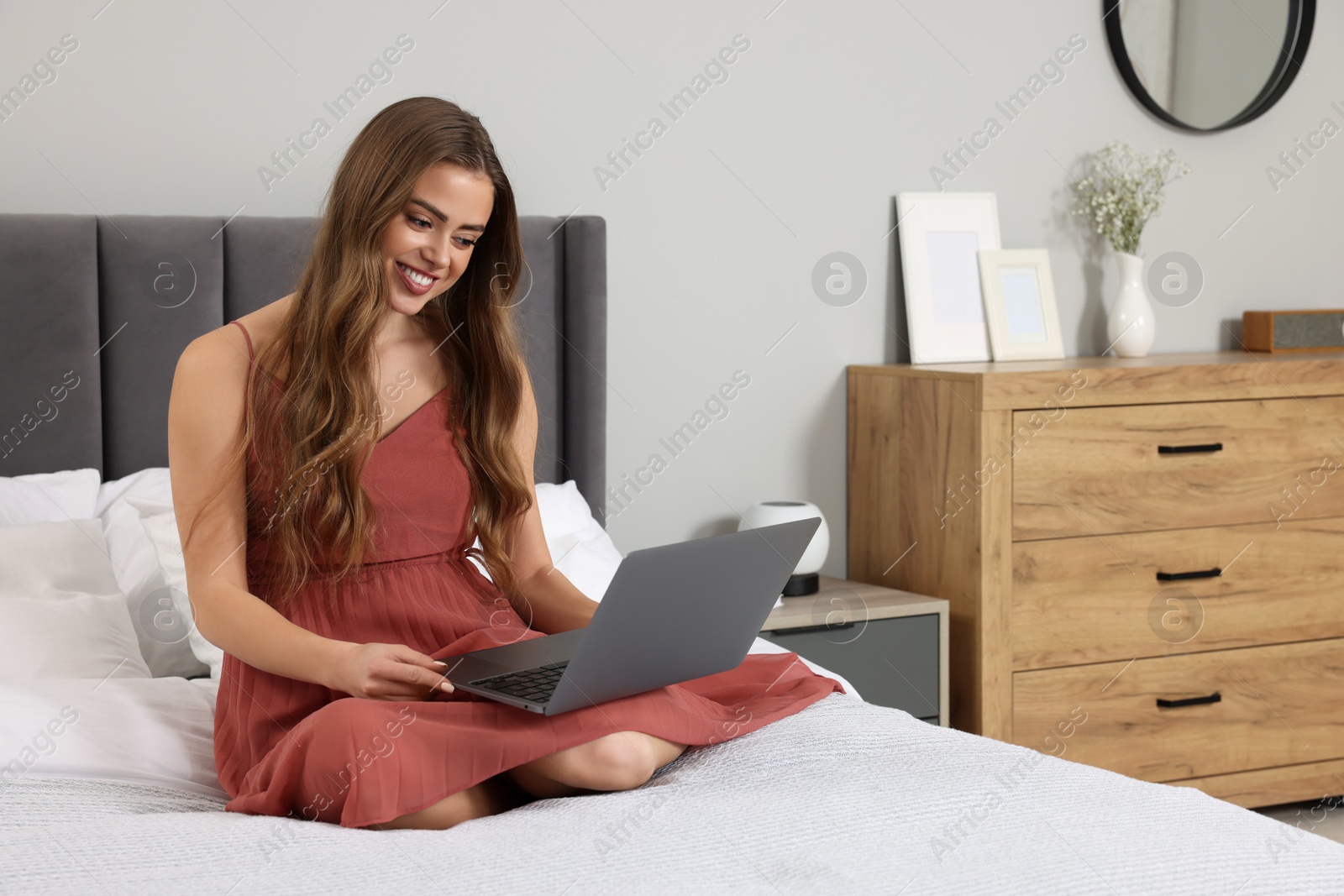 Photo of Happy woman with laptop on bed in bedroom